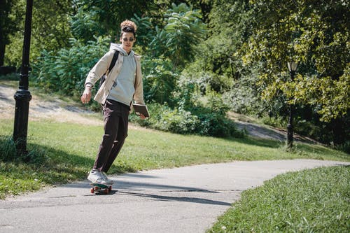 时髦的年轻种族人在公园的滑板上保持平衡 · 免费素材图片