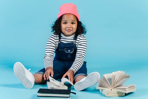 白色和黑色的条纹的长袖衬衫和粉红色的帽子，坐在白书上的女孩 · 免费素材图片