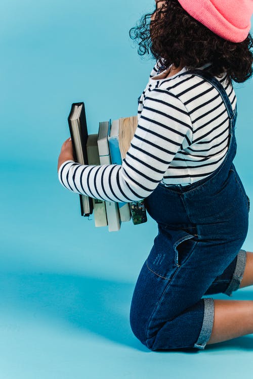 白色和黑色的条纹的长袖衬衫和蓝色牛仔牛仔裤，拿着本书的女人 · 免费素材图片