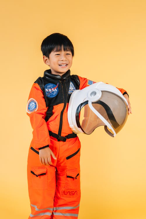 拿着白色和蓝色机器人玩具的橙色和黑色外套的男孩 · 免费素材图片
