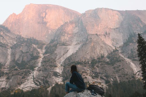 匿名的徒步旅行者在岩石峭壁上重建并在日落时欣赏山景 · 免费素材图片