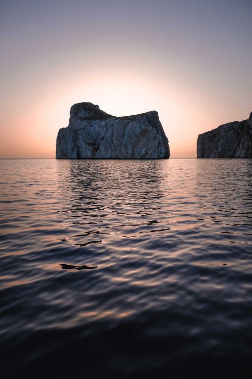 海洋与岩石峭壁上的落日的天空 · 免费素材图片