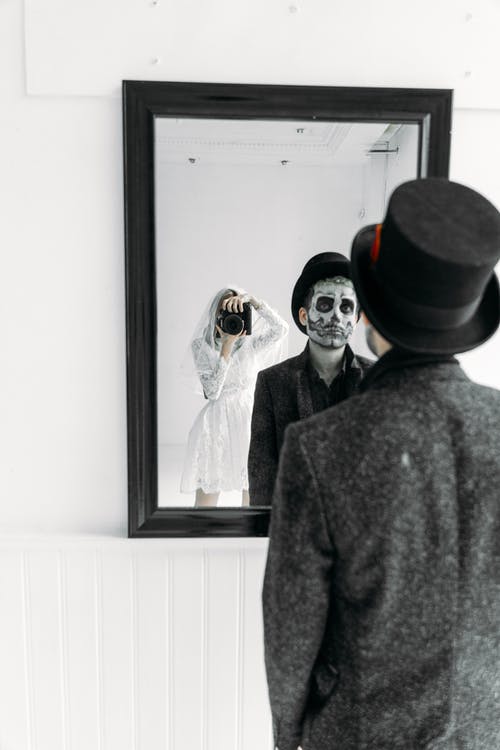 一个女人拿着照相机和一个男人站在镜子前的镜子里的倒影 · 免费素材图片
