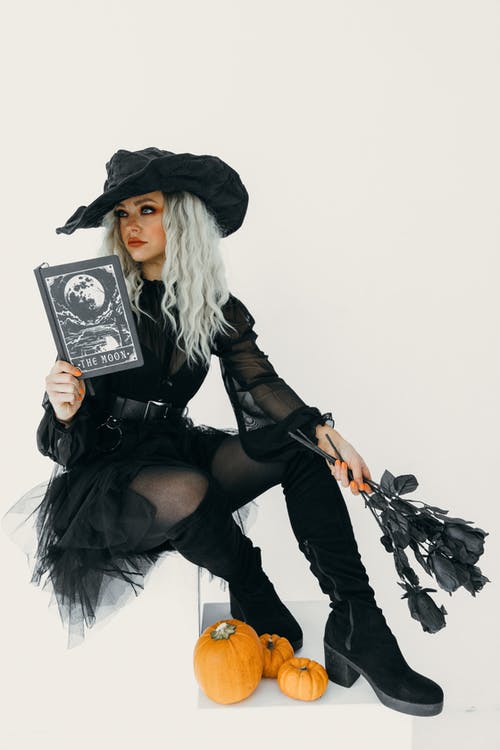 黑巫婆服装的妇女有一本书和在她的手上的黑玫瑰的 · 免费素材图片