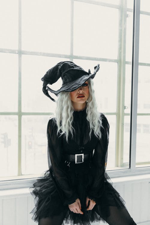 黑色女巫的帽子和裙子坐在窗户旁边的女人 · 免费素材图片