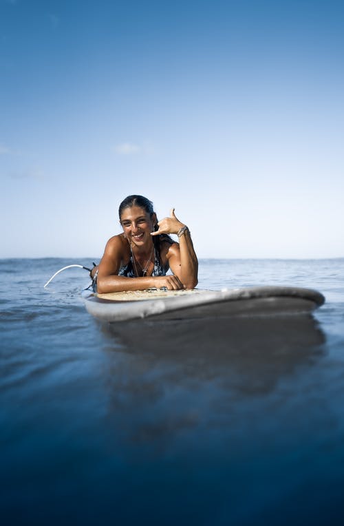 基于天蓝色的海表面的冲浪板上快乐的族裔女人 · 免费素材图片