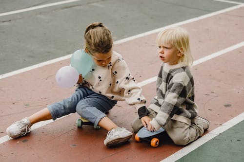 男孩和女孩坐在棕色的水泥地板上 · 免费素材图片