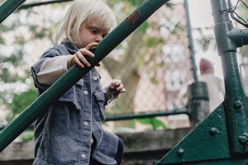 倚在绿色金属栅栏上的灰色外套的女孩 · 免费素材图片