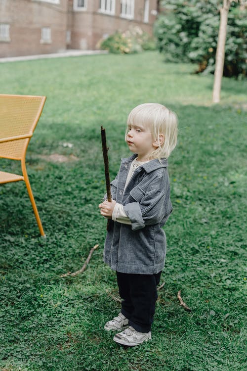 拿着棍子站立在绿草领域的灰色夹克的女孩 · 免费素材图片