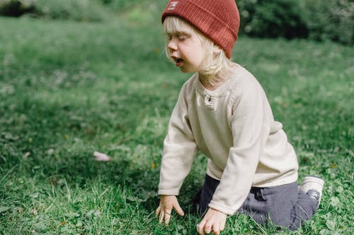 红色针织帽和米色毛衣坐在绿草上的孩子 · 免费素材图片