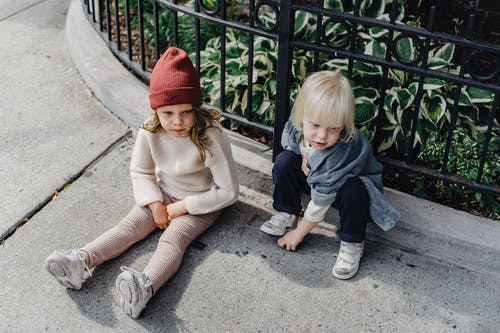 棕色毛衣和红色针织帽坐在灰色的水泥地板上的女孩 · 免费素材图片