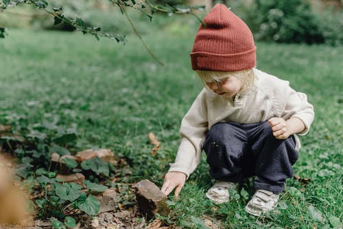 橙色编织帽和棕色夹克坐在绿草上的孩子 · 免费素材图片