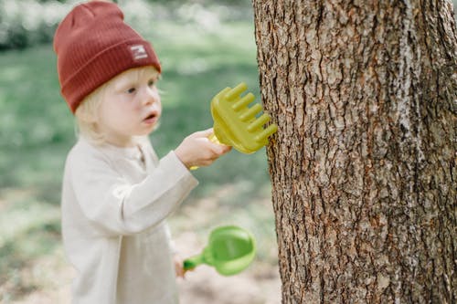 白色长袖衬衫和红色针织帽，拿着绿色的塑料铲子的孩子 · 免费素材图片