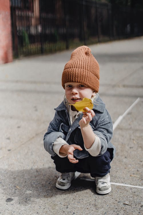 拿着黄色塑料玩具的灰色夹克和棕色针织帽的孩子 · 免费素材图片