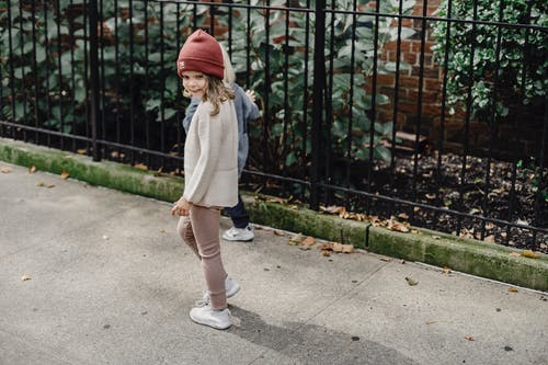 灰色外套和红色针织帽站在灰色的具体途径上的女孩 · 免费素材图片