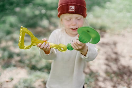红色的帽子，拿着绿色和黄色的塑料玩具的孩子 · 免费素材图片