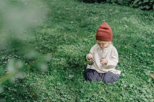 婴儿在橙色的针织帽和白色的长袖衬衫，坐在绿草地上 · 免费素材图片