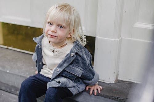 坐在灰色的水泥地板上的夹克和蓝色牛仔牛仔裤的灰色按钮的女孩 · 免费素材图片