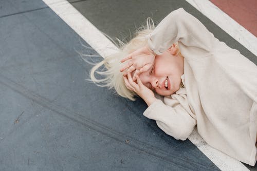 躺在灰色的水泥地板上的白色长袖衬衫的女人 · 免费素材图片