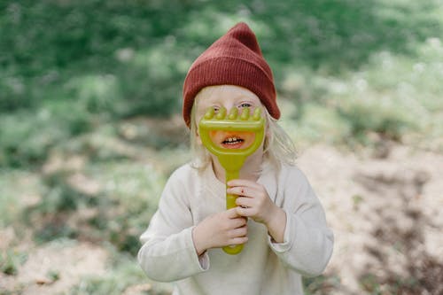 拿着绿色和黄色的塑料玩具的白毛衣的女孩 · 免费素材图片