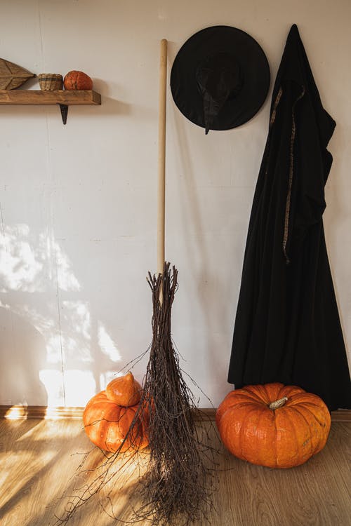 黑色女巫服装和一把扫帚旁边的橙色南瓜 · 免费素材图片