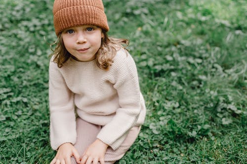 坐在绿色的草地上的白色毛衣和棕色针织帽的女孩 · 免费素材图片