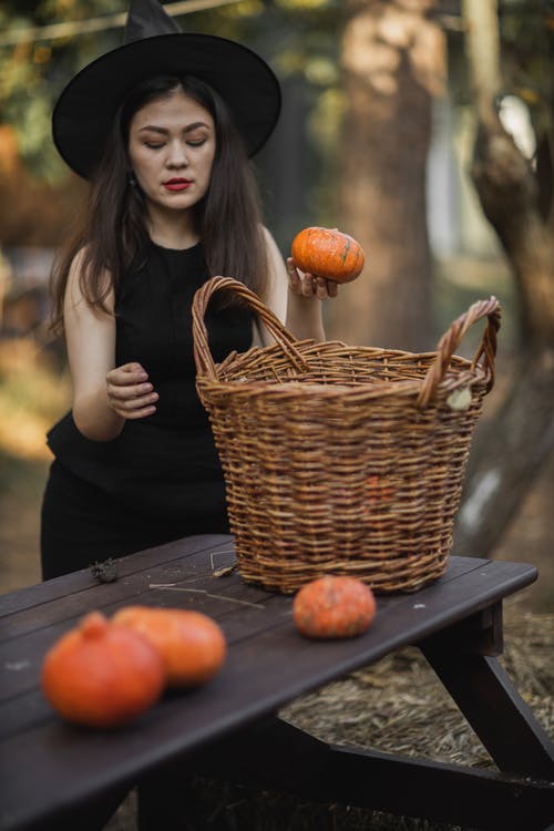 拿着南瓜在棕色被编织的篮子旁边的黑礼服的妇女南瓜 · 免费素材图片