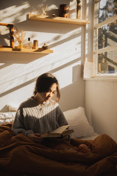 坐在她床上看书的灰色长袖衬衫的女人 · 免费素材图片