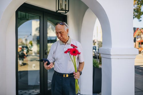 老人拿着红色的花，在他的智能手机上发短信 · 免费素材图片