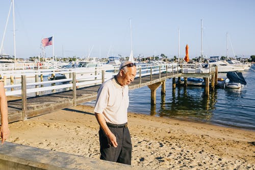 白船员的脖子t恤和黑色的裤子，站在海滩上的人 · 免费素材图片