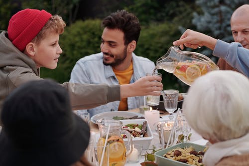 人在户外家庭晚餐期间向男孩倒柠檬水 · 免费素材图片