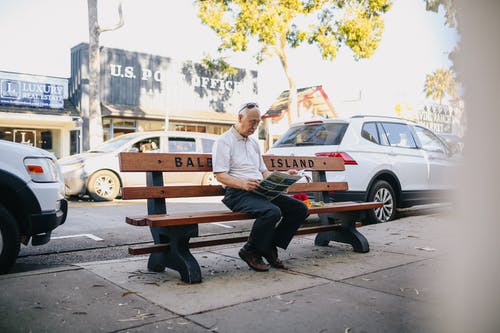 老人坐在长椅上看报纸 · 免费素材图片