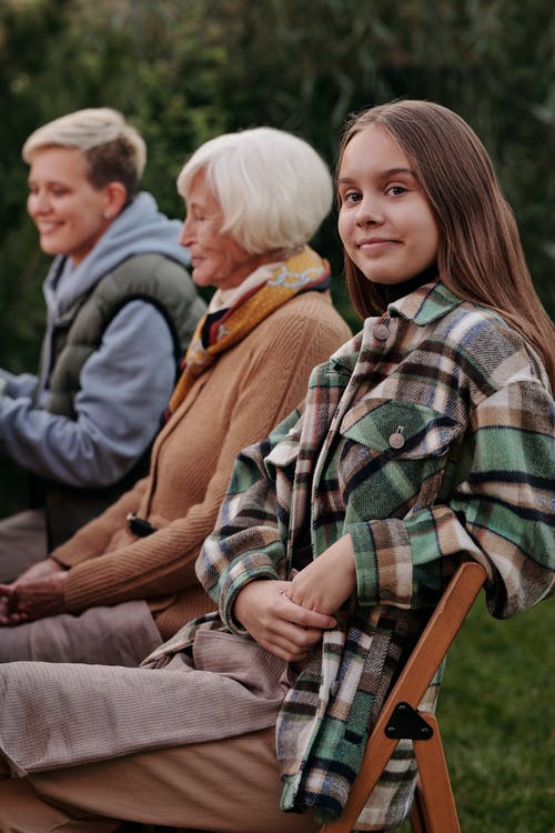 倾斜在椅子的十几岁的女孩在亲戚旁边户外 · 免费素材图片