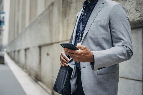 裁剪不露面的黑人商人，在人行道上使用智能手机 · 免费素材图片