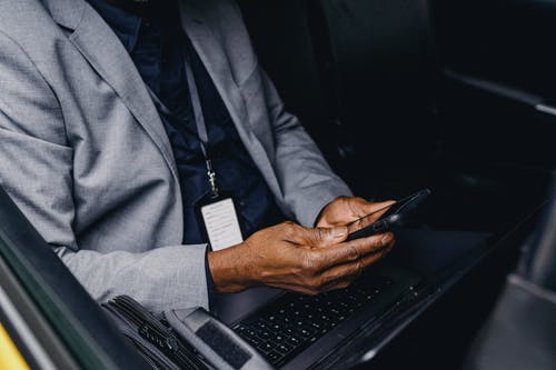 裁剪不露面的黑人商人，坐在车里和浏览智能手机 · 免费素材图片