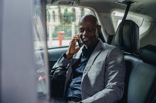 满意的黑人坐在汽车上，谈智能手机 · 免费素材图片