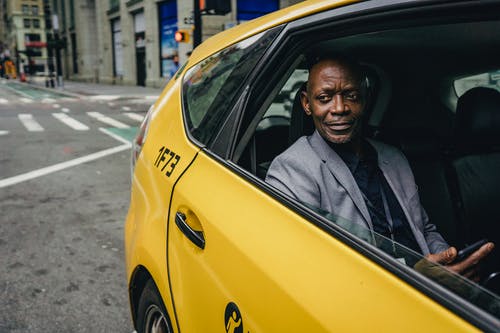 微笑在优雅的外套，与智能手机在出租车上的黑人 · 免费素材图片