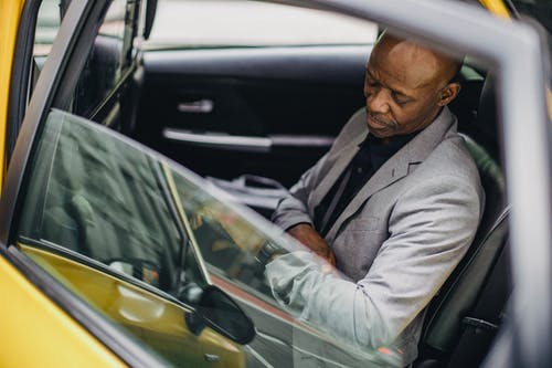 可敬的黑人商人坐在出租车和检查时间 · 免费素材图片