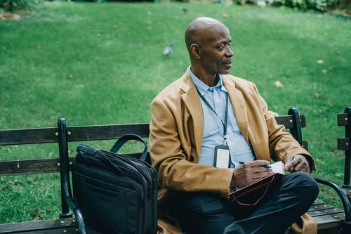 考虑黑人坐在公园的长椅上，用记事本 · 免费素材图片