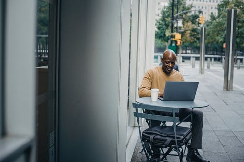 在人行道上咖啡馆的笔记本电脑上工作的严重族裔男子 · 免费素材图片