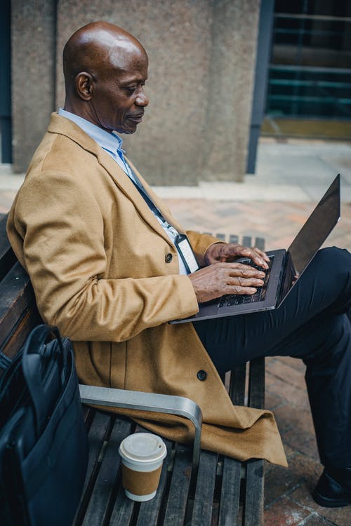 在长凳上使用笔记本电脑的严重黑商人 · 免费素材图片