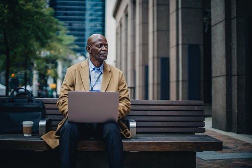 严重的黑人男性高管，笔记本电脑在街头的长椅上 · 免费素材图片