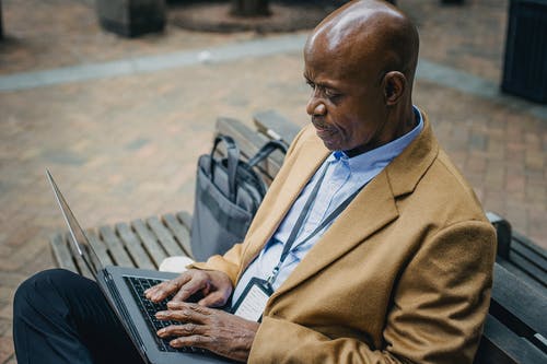 裁剪黑色商人坐在长椅上，使用笔记本电脑 · 免费素材图片