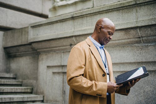集中成熟的非洲裔美国商人，在老建筑附近的街道上阅读文件 · 免费素材图片