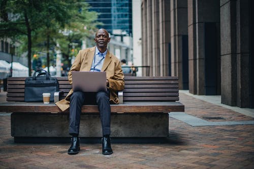 周到的黑商人坐在长凳上的笔记本电脑 · 免费素材图片