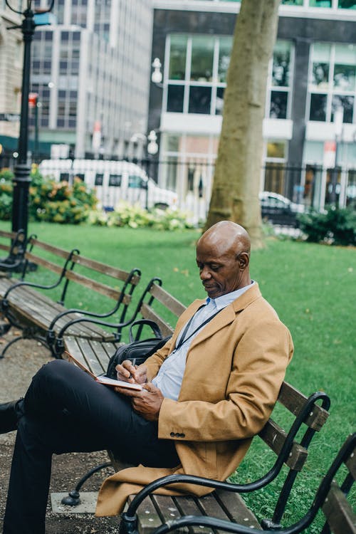 集中黑人坐在长椅上，写在笔记本上 · 免费素材图片