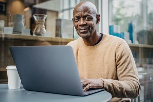 微笑中间岁黑人在咖啡馆上网本上远程工作 · 免费素材图片
