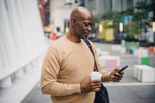 沉思成熟的黑人男性，外卖咖啡在大街上使用智能手机 · 免费素材图片