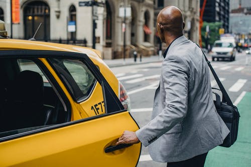 匿名的黑人男子在繁忙的街道上打开出租车门 · 免费素材图片