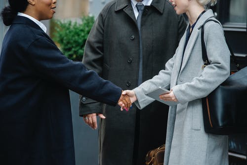 多种族的妇女，在时髦的外套，在男人附近握手 · 免费素材图片